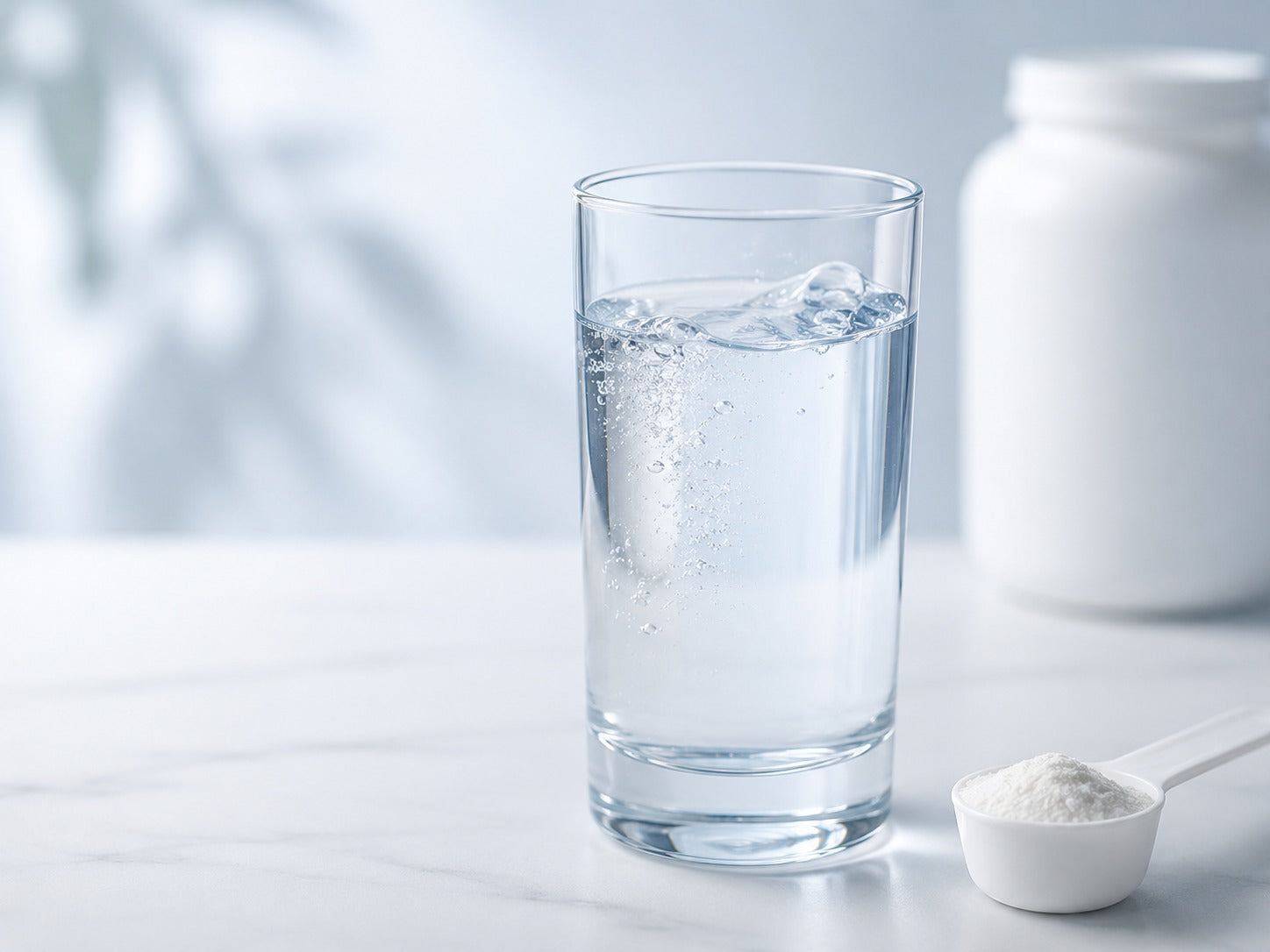 A glass of water with a white bottle in the background and a scoop of powder in the foreground